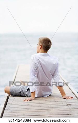 Back view of a young man sitting and relaxing in a Pier View Large Photo Image Picture - Back view of a young man sitting and relaxing in a Pier. Fotosearch