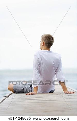 Back view of a young man sitting and relaxing in a Pier View Large Photo Image Stock Photography - Back view of a young man sitting and relaxing in a Pier. Fotosearch