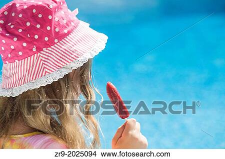 Back view of girl wearing polka dot hat eating a popsicle. View Large Photo Image Picture - Back view of girl wearing polka dot hat eating a popsicle.. Fotosearch