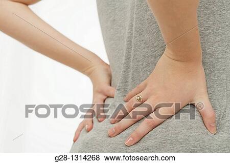 back view of young woman holding her back with her 2 hands dressed in grey detail View Large Photo Image Stock Photo - back view of young woman holding her back with her 2 hands dressed in grey detail. Fotosearch
