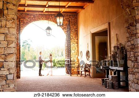 Stock Photograph - Backlit couple holding hands in the sunfilled doorway of a winery in Franschhoek, South Africa.. Fotosearch