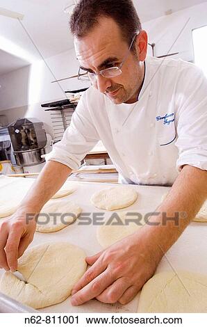 Stock Image - baker cutting the dough to make bread in the oven. Fotosearch