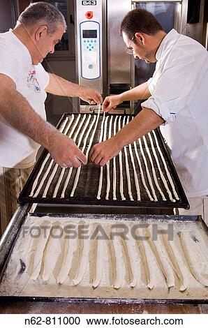 Stock Image - baker prepares bread sticks to put them in the oven. Fotosearch