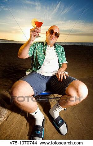 Bald guy on holidays sitting on a sunny beach holding a cocktail View Large Photo Image Picture - Bald guy on holidays sitting on a sunny beach holding a cocktail. Fotosearch