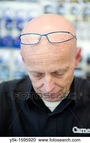 Bald salesman of a Rotterdam camerastore with glasses looking down. View Large Photo Image Stock Image - Bald salesman of a Rotterdam camerastore with glasses looking down.. Fotosearch