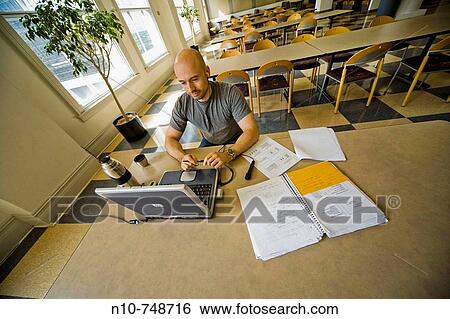 Balding young man working on his laptop computer in the dining area at his college. View Large Photo Image Stock Photograph - Balding young man working on his laptop computer in the dining area at his college.. Fotosearch