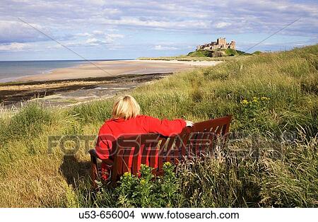 Bamburgh Beach and Castle, with woman wearing a red jacket seated in the foreground, Northumberland, England, UK View Large Photo Image Picture - Bamburgh Beach and Castle, with woman wearing a red jacket seated in the foreground, Northumberland, England, UK. Fotosearch