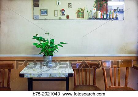 Stock Image - Bar table with plant, three chairs to the side and a mirror on the wall, Paris, France, Europe.. Fotosearch