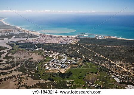 Picture - Barbate de Franco CBdiz, Spain Aerial view The city and its little harbour The river mouth throw browny water into the sea Salt lakes on the left Tanger Marroco on the Horizon line.. Fotosearch