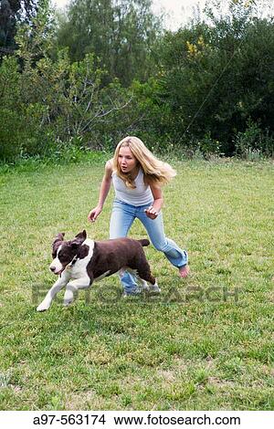 Barefoot blonde teen girl in blue jeans and white tank top running with pet dog on a grass lawn. View Large Photo Image Picture - Barefoot blonde teen girl in blue jeans and white tank top running with pet dog on a grass lawn.. Fotosearch