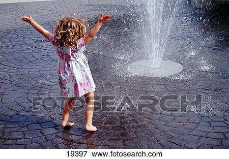 Barefoot little girl with curly hair, in dress, arms wide, enjoying spray from street-level fountain View Large Photo Image Stock Photo - Barefoot little girl with curly hair, in dress, arms wide, enjoying spray from street-level fountain. Fotosearch
