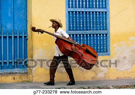 Stock Photo - Bass Player carrying his instrument in a Street of Trinidad de Cuba. Cuba. Fotosearch