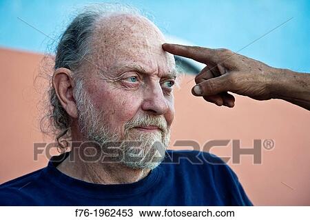 Stock Image - Bearded man in his sixties being touched on the forehead by another man's finger.. Fotosearch