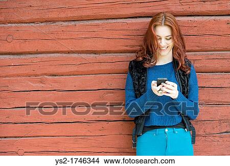 Beatiful young woman with red hair smiling and looking at her mobile phone View Large Photo Image Picture - Beatiful young woman with red hair smiling and looking at her mobile phone. Fotosearch