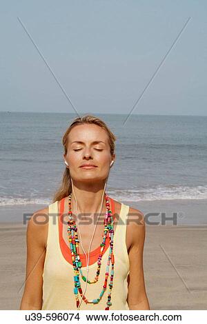 Beautiful blonde woman standing on a beach in India listening to headphones with her eyes closed. View Large Photo Image Picture - Beautiful blonde woman standing on a beach in India listening to headphones with her eyes closed.. Fotosearch