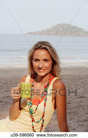 Beautiful blonde woman wearing a yellow vest sat on a beach in India and drinking a cup of coffee. View Large Photo Image Stock Image - Beautiful blonde woman wearing a yellow vest sat on a beach in India and drinking a cup of coffee.. Fotosearch