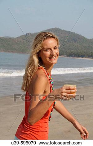 Beautiful blonde woman wearing an orange vest and drinking a glass of orange juice on a beach in India. View Large Photo Image Stock Image - Beautiful blonde woman wearing an orange vest and drinking a glass of orange juice on a beach in India.. Fotosearch