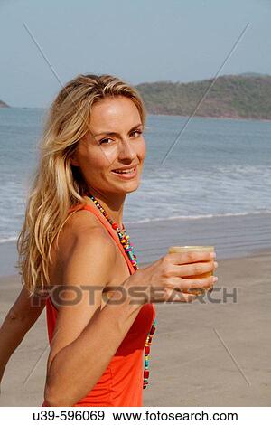 Beautiful blonde woman wearing an orange vest and drinking a glass of orange juice on a beach in India. View Large Photo Image Stock Photo - Beautiful blonde woman wearing an orange vest and drinking a glass of orange juice on a beach in India.. Fotosearch