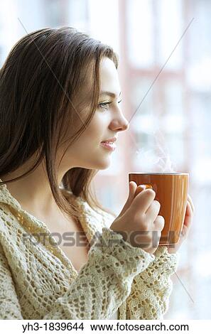 Beautiful young girl drinking hot tea while looking at the window View Large Photo Image Picture - Beautiful young girl drinking hot tea while looking at the window. Fotosearch