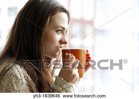 Beautiful young girl drinking hot tea while looking at the window View Large Photo Image Stock Photograph - Beautiful young girl drinking hot tea while looking at the window. Fotosearch