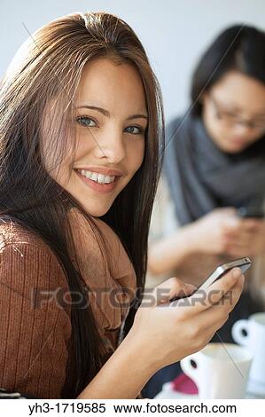 Beautiful young girl smiling in front of the camera while holding a smartphone View Large Photo Image Stock Photography - Beautiful young girl smiling in front of the camera while holding a smartphone. Fotosearch