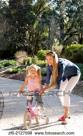 Stock Photo - beautiful young mother and daughter riding bike and having fun outside in a park.. Fotosearch