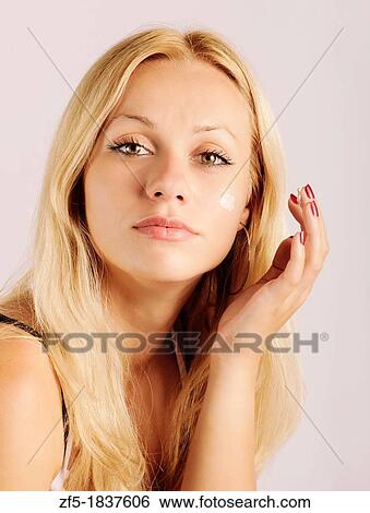 Stock Photograph - Beautiful young woman applying face cream. Fotosearch