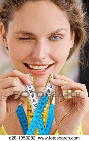 beautiful young woman winking at photographer, holding a tape maesure and smiling View Large Photo Image Stock Image - beautiful young woman winking at photographer, holding a tape maesure and smiling. Fotosearch