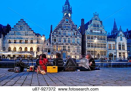 Stock Image - Belgium, Flanders, Ghent, Friends Sitting on Waterfront Leie River at Dusk. Fotosearch