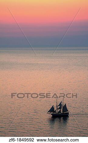 Big masked sailboat sailing in sunset of beautiful Oia in Santorini Greece in Greek Islands from above on cliff into water View Large Photo Image Stock Image - Big masked sailboat sailing in sunset of beautiful Oia in Santorini Greece in Greek Islands from above on cliff into water. Fotosearch