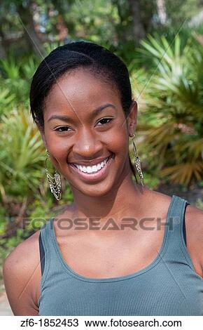 Stock Image - Black African American girl aged 18 portrait in yard outdoors laughing. Fotosearch