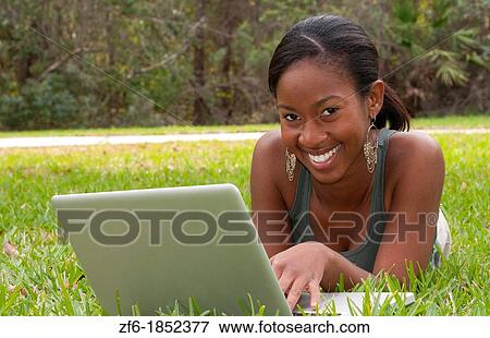 Stock Photo - Black African American teen girl age 18 working on computer facebook with emailing friends in front yard on grass. Fotosearch