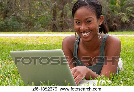 Stock Photo - Black African American teen girl age 18 working on computer facebook with emailing friends in front yard on grass. Fotosearch