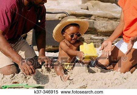 Stock Photography - Black family on the beach with young boy building sandcastle.. Fotosearch