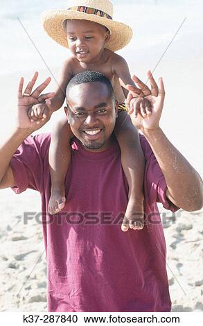 Black father with son wearing bathing trunks sitting on his shoulders at the beach on vacation View Large Photo Image Stock Image - Black father with son wearing bathing trunks sitting on his shoulders at the beach on vacation. Fotosearch