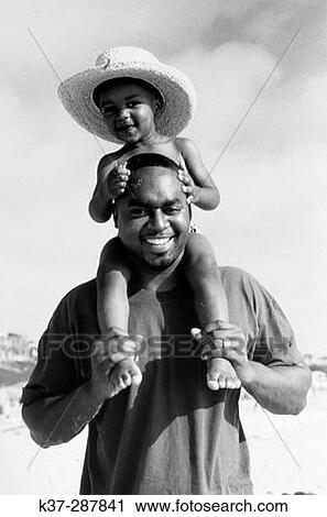 Black father with son wearing bathing trunks sitting on his shoulders at the beach on vacation View Large Photo Image Stock Image - Black father with son wearing bathing trunks sitting on his shoulders at the beach on vacation. Fotosearch