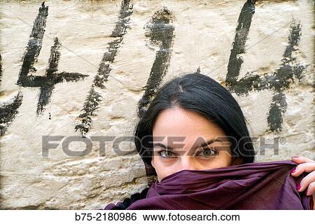 Black hair young woman looking at the camera against a wall with graffiti and covering his face with a pamina in the Medina of Fez, Morocco, Africa. View Large Photo Image Stock Photograph - Black hair young woman looking at the camera against a wall with graffiti and covering his face with a pamina in the Medina of Fez, Morocco, Africa.. Fotosearch