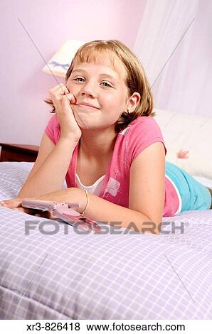 Stock Photo - Blond female child with cell phone laying on bed. Fotosearch