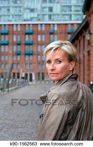 Blond haired executive woman, turning her head and looking back over her shoulder, seen from backside, with office building made of red bricks, windows and balconies in the background, Hamburg, Germany, Europe View Large Photo Image Stock Image - Blond haired executive woman, turning her head and looking back over her shoulder, seen from backside, with office building made of red bricks, windows and balconies in the background, Hamburg, Germany, Europe. Fotosearch