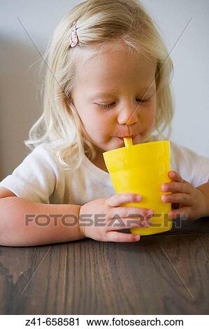 Stock Image - Blond little girl is drinking from a yellow cup. Fotosearch