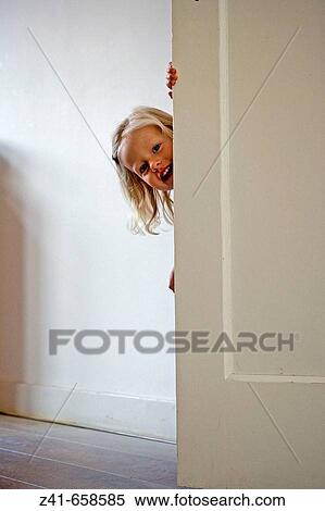 Stock Photography - Blond little girl is hiding behind a door. Fotosearch