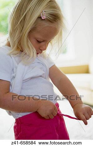 Picture - Blond little girl is trying to dress. Fotosearch