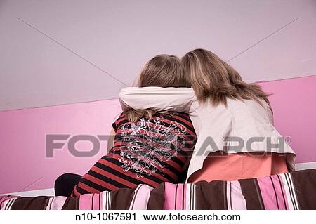 Stock Image - Blond preteen sisters on a bed. Fotosearch