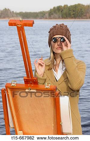 Blond woman in her 20's 30's painting by the lake using a pair of binoculars View Large Photo Image Stock Image - Blond woman in her 20's 30's painting by the lake using a pair of binoculars. Fotosearch