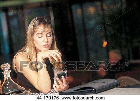 Stock Photograph - Blond woman sitting in a bar with glass of wine and electronic organizer. Fotosearch