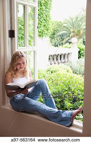 Blonde barefoot teen girl sits by an open window reading a book. View Large Photo Image Picture - Blonde barefoot teen girl sits by an open window reading a book.. Fotosearch