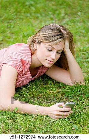 Picture - Blonde beautiful woman writting a SMS lying down in the park. Fotosearch