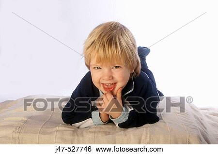 Stock Photograph - blonde haired, 3 year old boy laughing into camera, lying on his tummy. Fotosearch