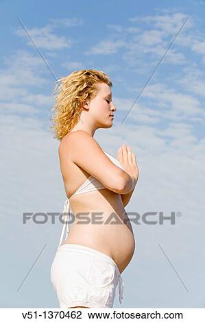 Stock Image - Blonde pregnant woman doing yoga at the beach. Fotosearch