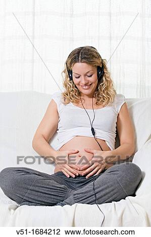 Stock Image - Blonde pregnant woman sitting on the sofa. Fotosearch